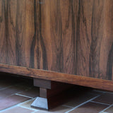 Grande enfilade vintage en palissandre de 240 cm, placage au fil en miroir, deux caissons fermant à clé de part et d'autre d'une niche centrale ouverte, tablettes intérieures en bois clair, reposant sur deux pieds pleins posés en retrait