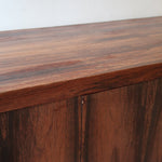Grande enfilade vintage en palissandre de 240 cm, placage au fil en miroir, deux caissons fermant à clé de part et d'autre d'une niche centrale ouverte, tablettes intérieures en bois clair, reposant sur deux pieds pleins posés en retrait