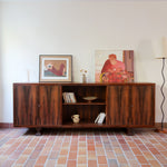 Grande enfilade vintage en palissandre de 240 cm, placage au fil en miroir, deux caissons fermant à clé de part et d'autre d'une niche centrale ouverte, tablettes intérieures en bois clair, reposant sur deux pieds pleins posés en retrait