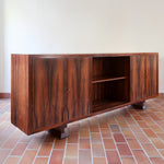 Grande enfilade vintage en palissandre de 240 cm, placage au fil en miroir, deux caissons fermant à clé de part et d'autre d'une niche centrale ouverte, tablettes intérieures en bois clair, reposant sur deux pieds pleins posés en retrait