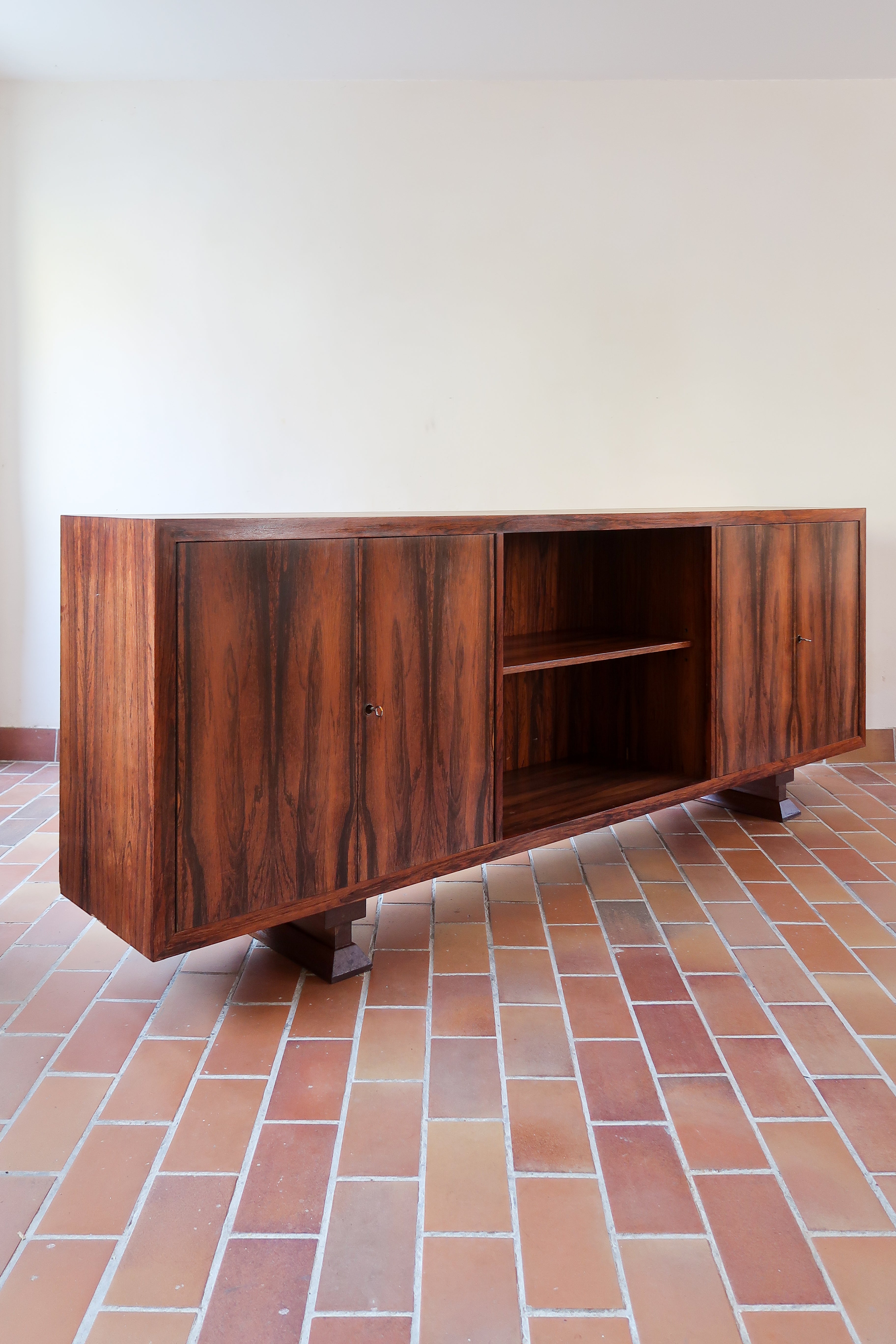 Grande enfilade vintage en palissandre de 240 cm, placage au fil en miroir, deux caissons fermant à clé de part et d'autre d'une niche centrale ouverte, tablettes intérieures en bois clair, reposant sur deux pieds pleins posés en retrait