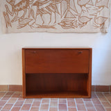 Meuble bar vintage en bois de teck, années 90, abattant sur deux compas chromés découvrant un intérieur doublé de verre noir, poignée sculptée dans la masse, niche basse ouverte sur toute la largeur