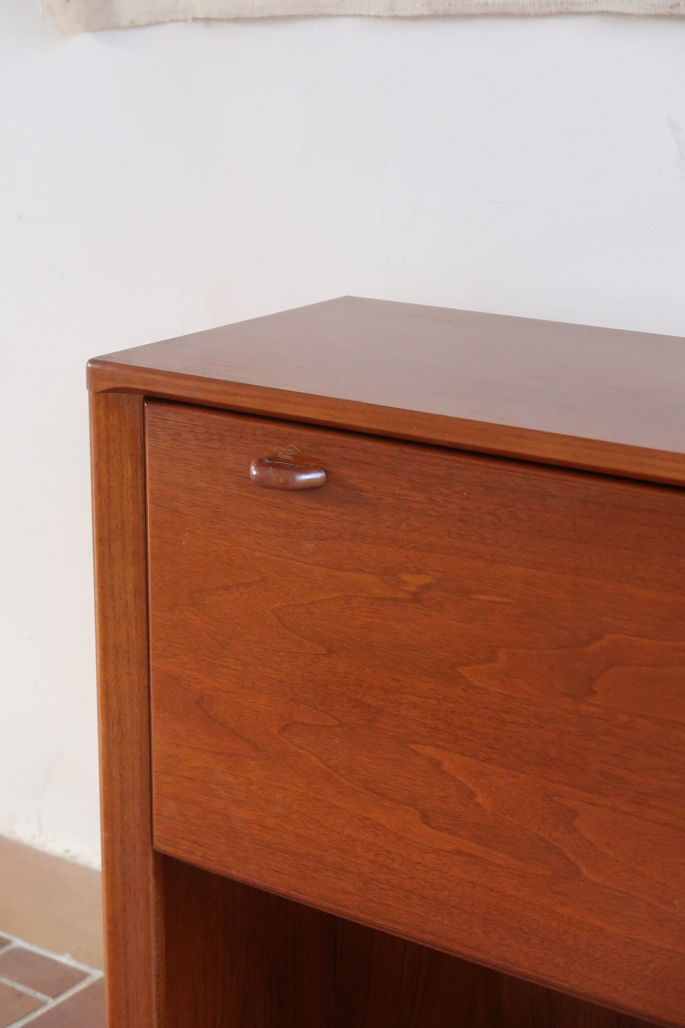 Meuble bar vintage en bois de teck, années 90, abattant sur deux compas chromés découvrant un intérieur doublé de verre noir, poignée sculptée dans la masse, niche basse ouverte sur toute la largeur