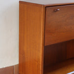 Meuble bar vintage en bois de teck, années 90, abattant sur deux compas chromés découvrant un intérieur doublé de verre noir, poignée sculptée dans la masse, niche basse ouverte sur toute la largeur