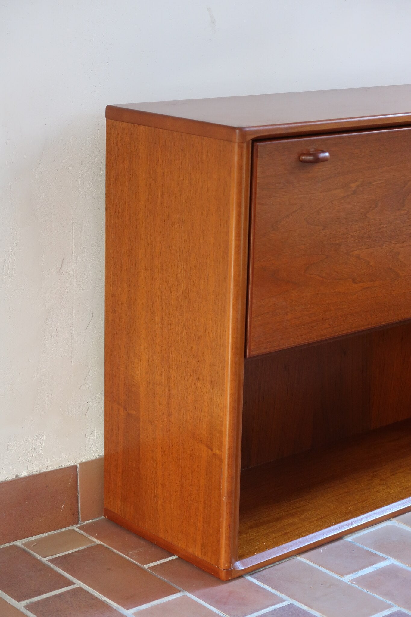 Meuble bar vintage en bois de teck, années 90, abattant sur deux compas chromés découvrant un intérieur doublé de verre noir, poignée sculptée dans la masse, niche basse ouverte sur toute la largeur