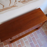 Meuble bar vintage en bois de teck, années 90, abattant sur deux compas chromés découvrant un intérieur doublé de verre noir, poignée sculptée dans la masse, niche basse ouverte sur toute la largeur