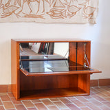 Meuble bar vintage en bois de teck, années 90, abattant sur deux compas chromés découvrant un intérieur doublé de verre noir, poignée sculptée dans la masse, niche basse ouverte sur toute la largeur