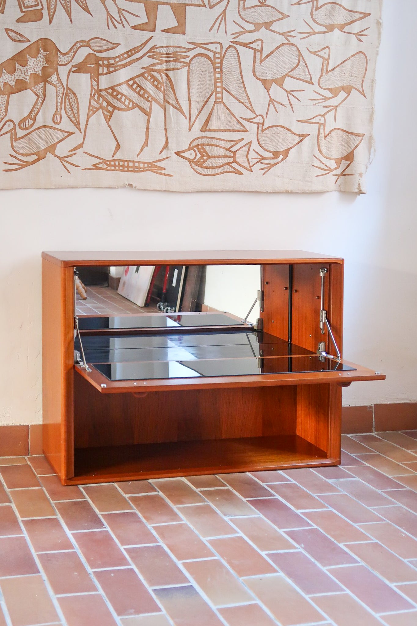 Meuble bar vintage en bois de teck, années 90, abattant sur deux compas chromés découvrant un intérieur doublé de verre noir, poignée sculptée dans la masse, niche basse ouverte sur toute la largeur
