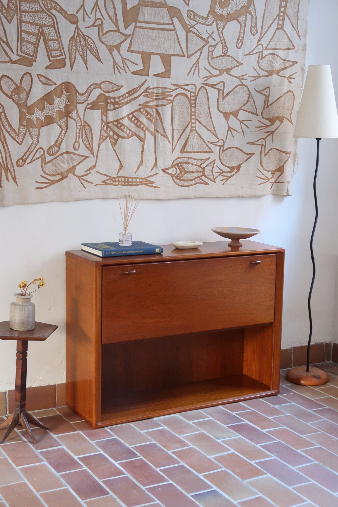 Meuble bar vintage en bois de teck, années 90, abattant sur deux compas chromés découvrant un intérieur doublé de verre noir, poignée sculptée dans la masse, niche basse ouverte sur toute la largeur