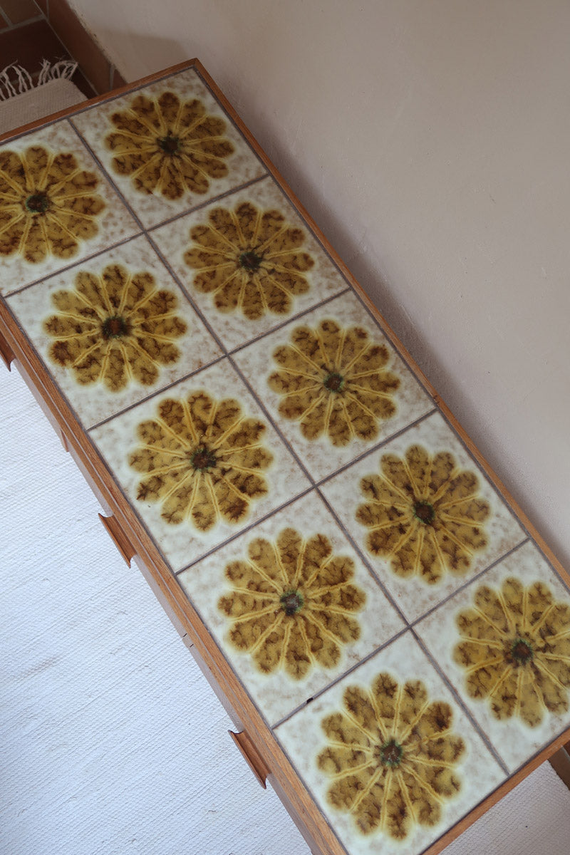 Meuble TV vintage en bois des années 70 avec plateau en céramique à motif floral, trois tiroirs et niches ouvertes.