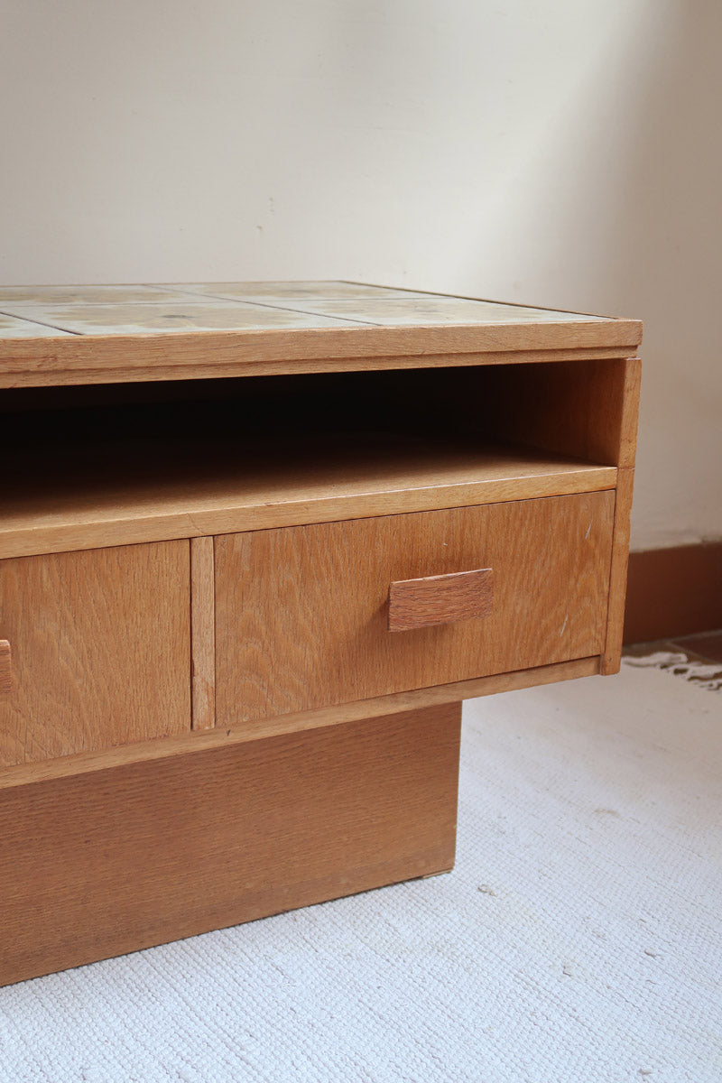 Meuble TV vintage en bois des années 70 avec plateau en céramique à motif floral, trois tiroirs et niches ouvertes.