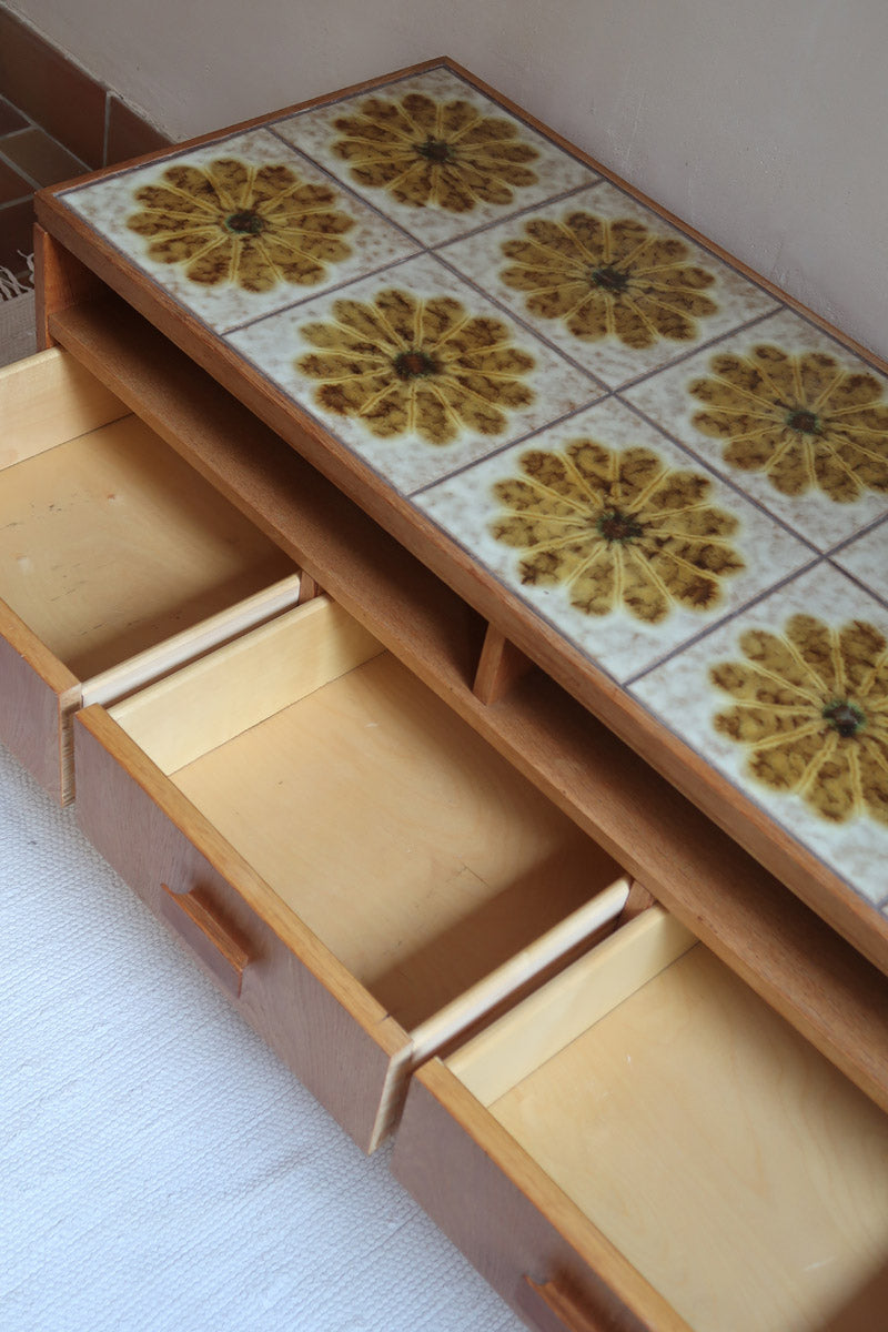 Meuble TV vintage en bois des années 70 avec plateau en céramique à motif floral, trois tiroirs et niches ouvertes.