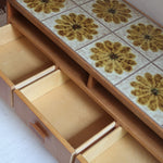 Meuble TV vintage en bois des années 70 avec plateau en céramique à motif floral, trois tiroirs et niches ouvertes.