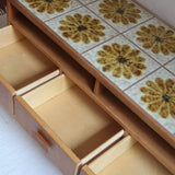 Meuble TV vintage en bois des années 70 avec plateau en céramique à motif floral, trois tiroirs et niches ouvertes.
