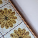 Meuble TV vintage en bois des années 70 avec plateau en céramique à motif floral, trois tiroirs et niches ouvertes.