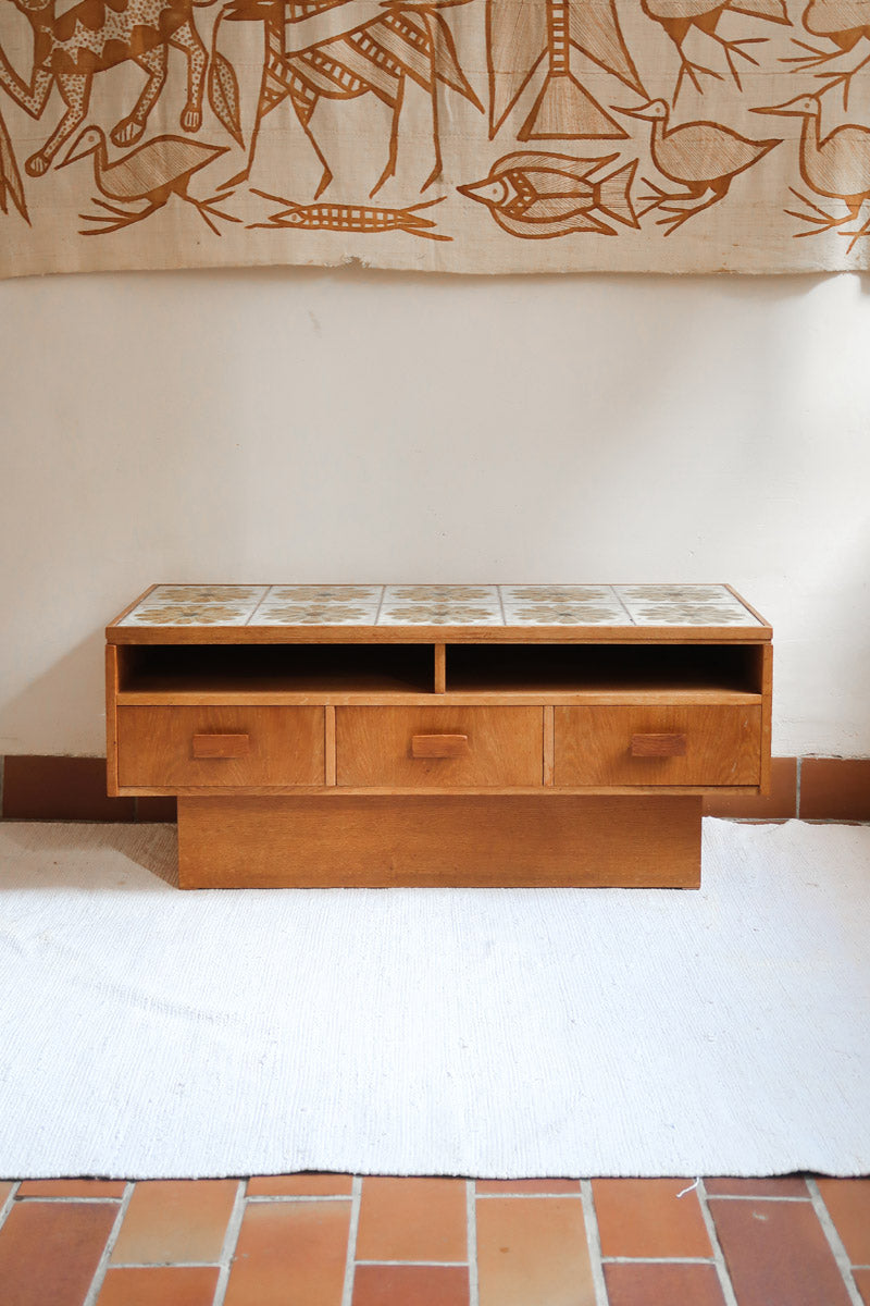 Meuble TV vintage en bois des années 70 avec plateau en céramique à motif floral, trois tiroirs et niches ouvertes.