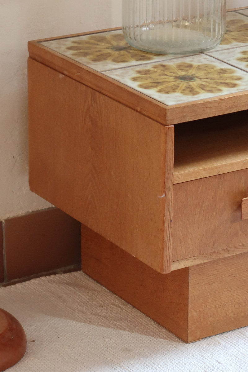 Meuble TV vintage en bois des années 70 avec plateau en céramique à motif floral, trois tiroirs et niches ouvertes.