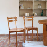 Paire de chaises vintage en hêtre massif, assise ronde et dossier à deux barreaux, style bistrot scandinave, présentées seules et en mise en situation.