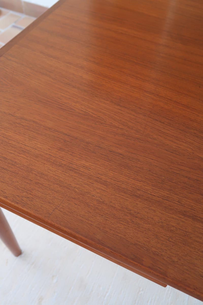 Table scandinave vintage en teck, années 60, extensible avec rallonge intégrée, pieds fuselés, quelques micro-rayures et pocs discrets visibles sur le plateau.