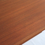 Table scandinave vintage en teck, années 60, extensible avec rallonge intégrée, pieds fuselés, quelques micro-rayures et pocs discrets visibles sur le plateau.