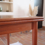 Table scandinave vintage en teck, années 60, extensible avec rallonge intégrée, pieds fuselés, quelques micro-rayures et pocs discrets visibles sur le plateau.