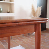 Table scandinave vintage en teck, années 60, extensible avec rallonge intégrée, pieds fuselés, quelques micro-rayures et pocs discrets visibles sur le plateau.