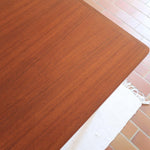 Table scandinave vintage en teck, années 60, extensible avec rallonge intégrée, pieds fuselés, quelques micro-rayures et pocs discrets visibles sur le plateau.