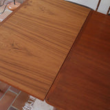 Table scandinave vintage en teck, années 60, extensible avec rallonge intégrée, pieds fuselés, quelques micro-rayures et pocs discrets visibles sur le plateau.