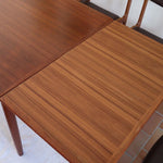 Table scandinave vintage en teck, années 60, extensible avec rallonge intégrée, pieds fuselés, quelques micro-rayures et pocs discrets visibles sur le plateau.
