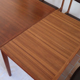 Table scandinave vintage en teck, années 60, extensible avec rallonge intégrée, pieds fuselés, quelques micro-rayures et pocs discrets visibles sur le plateau.