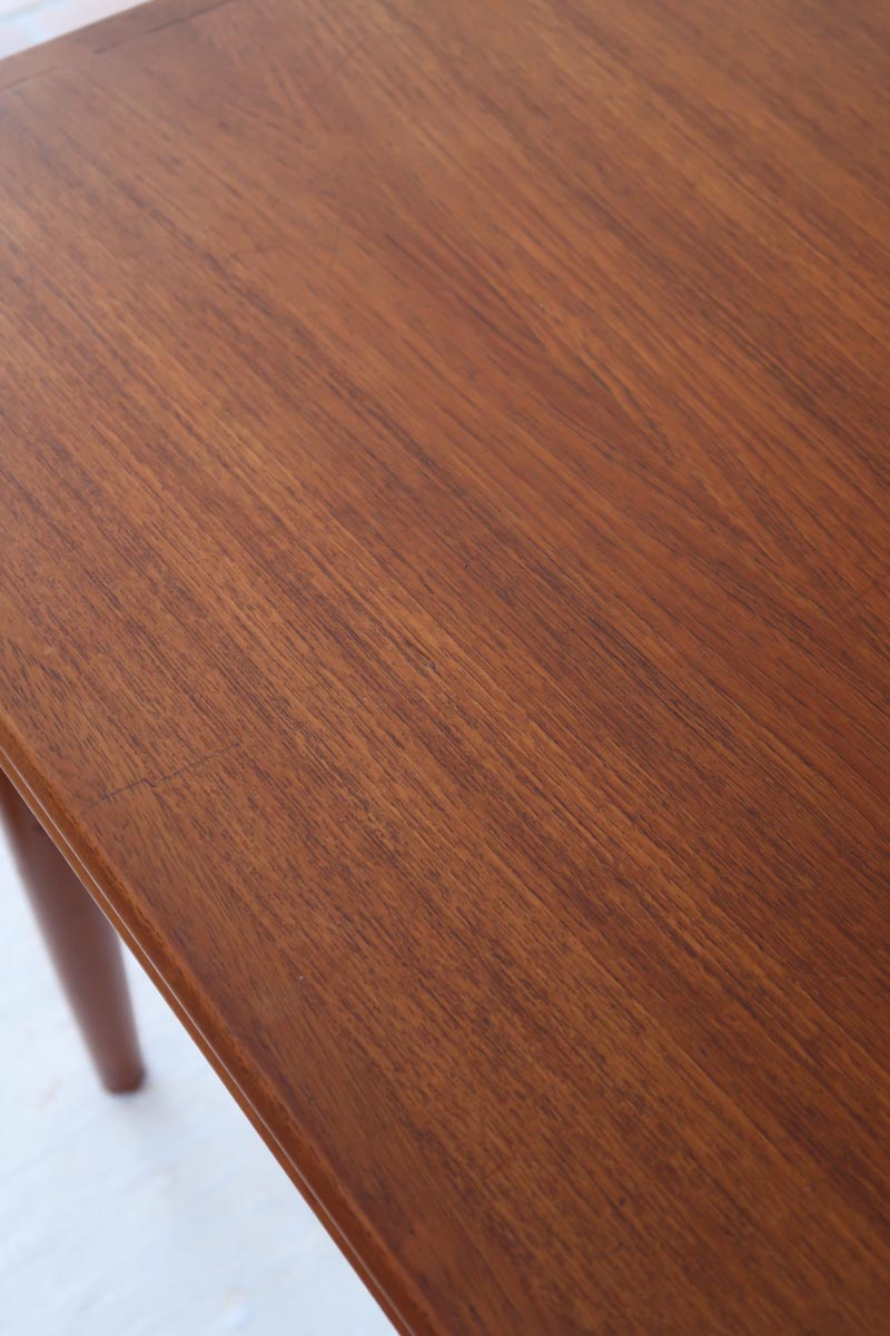 Table scandinave vintage en teck, années 60, extensible avec rallonge intégrée, pieds fuselés, quelques micro-rayures et pocs discrets visibles sur le plateau.