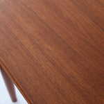 Table scandinave vintage en teck, années 60, extensible avec rallonge intégrée, pieds fuselés, quelques micro-rayures et pocs discrets visibles sur le plateau.