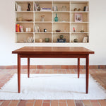 Table à manger scandinave en teck avec deux rallonges intégrées, design années 60, photographiée dans un intérieur lumineux.