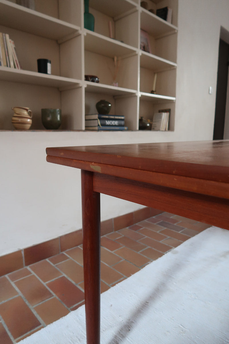 Table à manger scandinave en teck avec deux rallonges intégrées, design années 60, photographiée dans un intérieur lumineux.