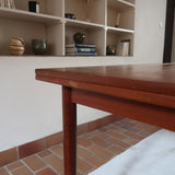 Table à manger scandinave en teck avec deux rallonges intégrées, design années 60, photographiée dans un intérieur lumineux.