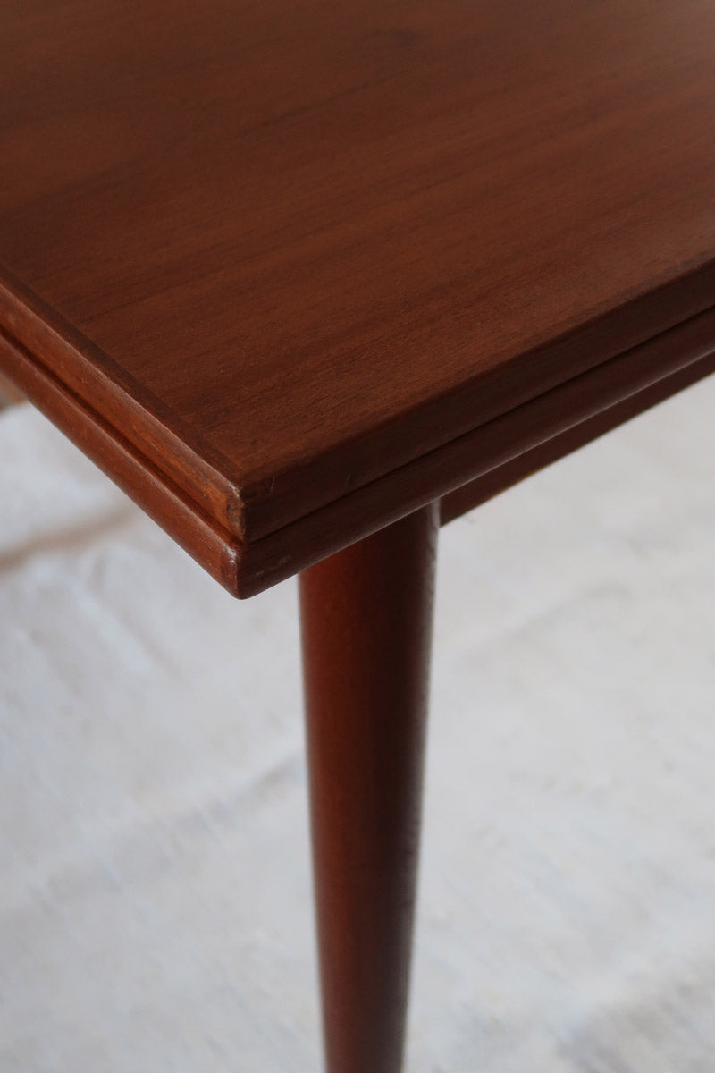 Table à manger scandinave en teck avec deux rallonges intégrées, design années 60, photographiée dans un intérieur lumineux.