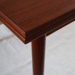 Table à manger scandinave en teck avec deux rallonges intégrées, design années 60, photographiée dans un intérieur lumineux.