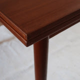 Table à manger scandinave en teck avec deux rallonges intégrées, design années 60, photographiée dans un intérieur lumineux.