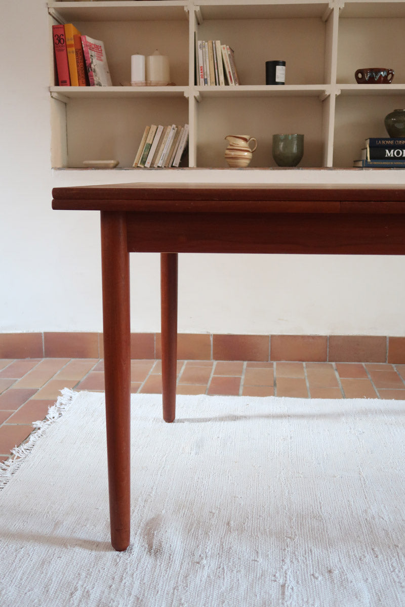 Table à manger scandinave en teck avec deux rallonges intégrées, design années 60, photographiée dans un intérieur lumineux.