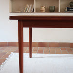 Table à manger scandinave en teck avec deux rallonges intégrées, design années 60, photographiée dans un intérieur lumineux.