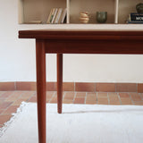 Table à manger scandinave en teck avec deux rallonges intégrées, design années 60, photographiée dans un intérieur lumineux.