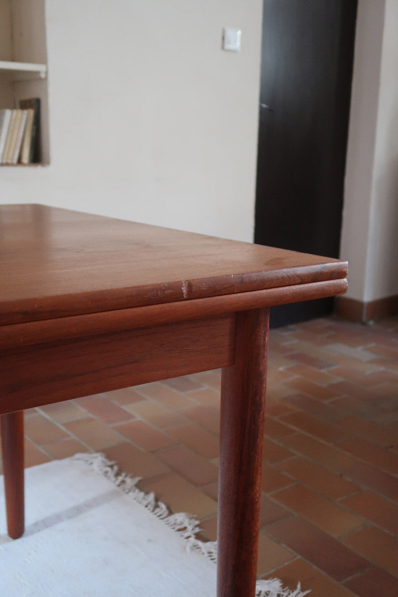 Table à manger scandinave en teck avec deux rallonges intégrées, design années 60, photographiée dans un intérieur lumineux.