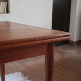 Table à manger scandinave en teck avec deux rallonges intégrées, design années 60, photographiée dans un intérieur lumineux.