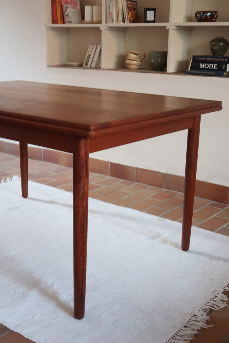 Table à manger scandinave en teck avec deux rallonges intégrées, design années 60, photographiée dans un intérieur lumineux.