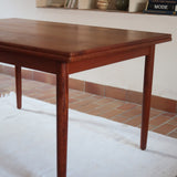 Table à manger scandinave en teck avec deux rallonges intégrées, design années 60, photographiée dans un intérieur lumineux.