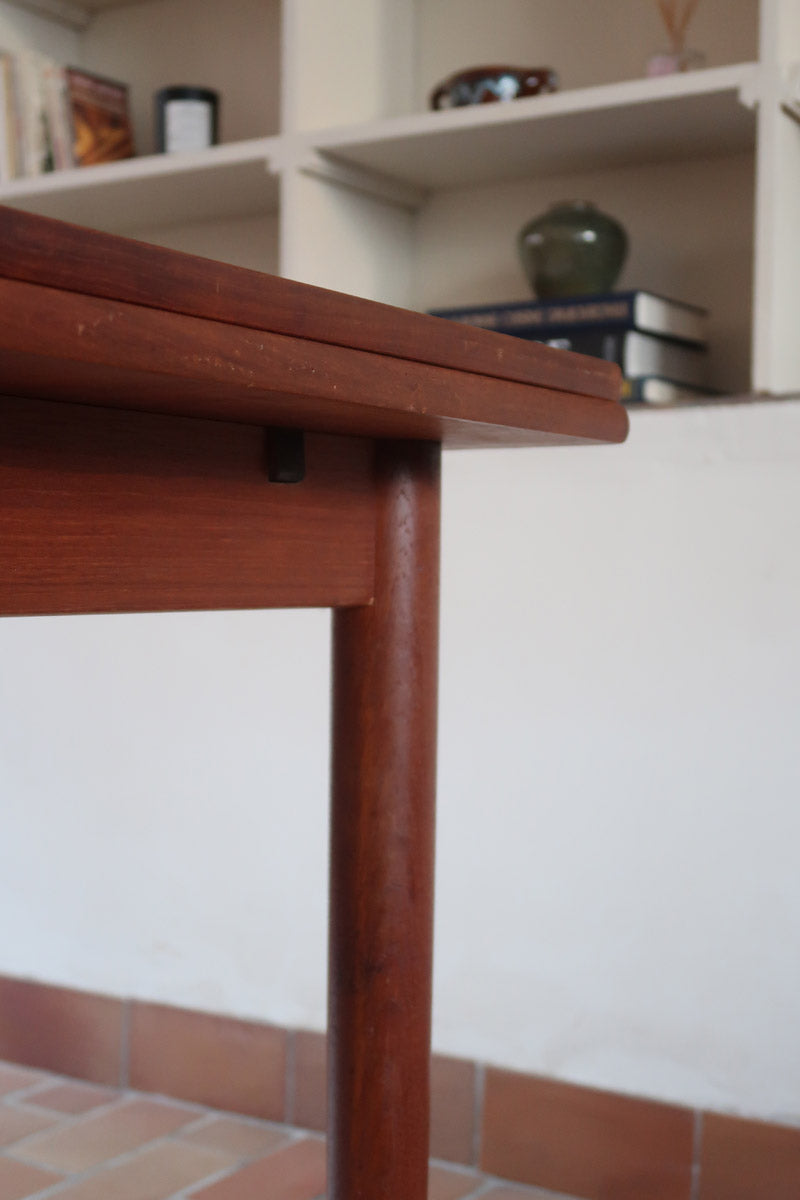 Table à manger scandinave en teck avec deux rallonges intégrées, design années 60, photographiée dans un intérieur lumineux.