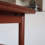 Table à manger scandinave en teck avec deux rallonges intégrées, design années 60, photographiée dans un intérieur lumineux.