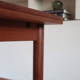 Table à manger scandinave en teck avec deux rallonges intégrées, design années 60, photographiée dans un intérieur lumineux.