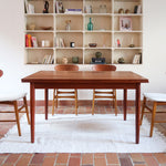 Table à manger scandinave en teck avec deux rallonges intégrées, design années 60, photographiée dans un intérieur lumineux.