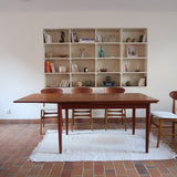 Table à manger scandinave en teck avec deux rallonges intégrées, design années 60, photographiée dans un intérieur lumineux.